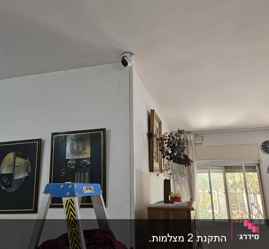 מצלמת אבטחה מותקנת בפינת תקרה בחדר עם סולם ותמונות
